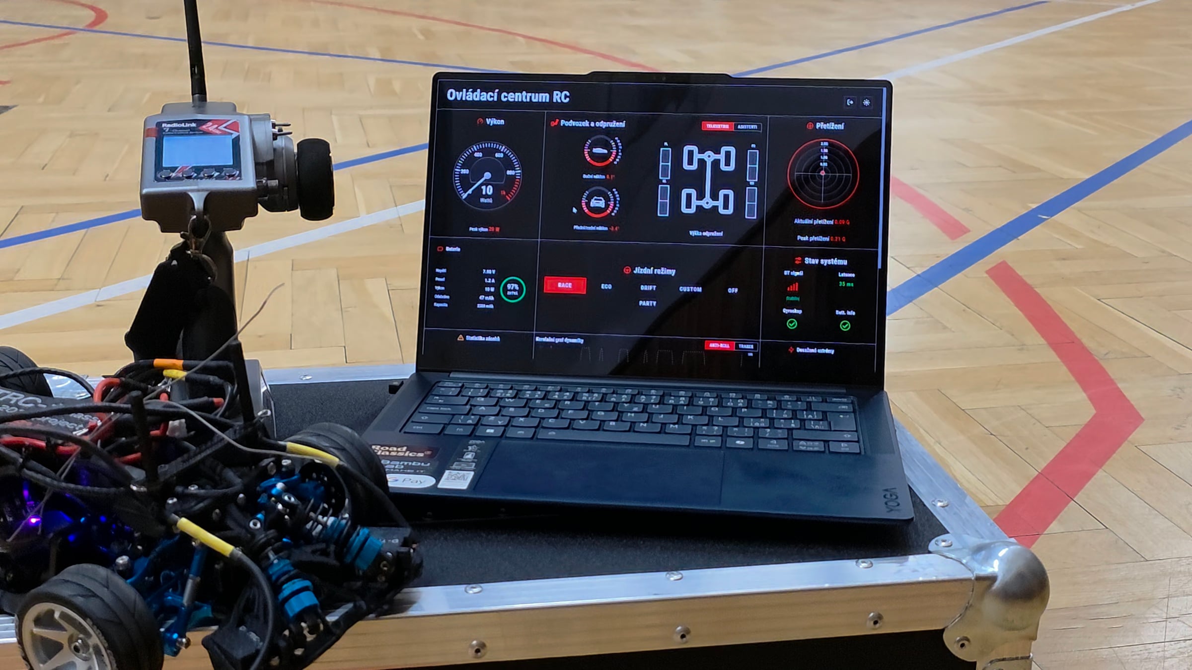 D-TRC-1 telemetrie — laptop s live dashboardem v popředí, auto rozostřené v pozadí, warm directional světlo